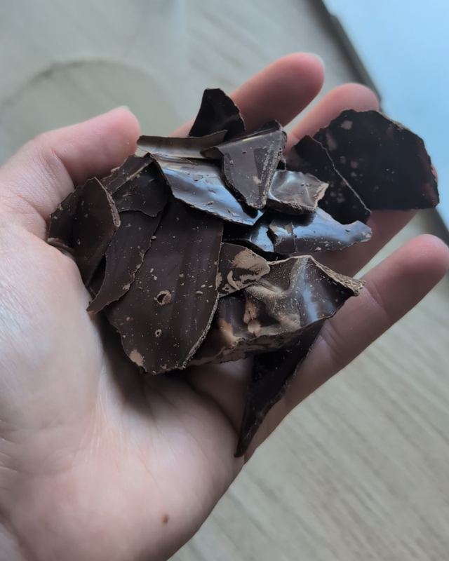Eine offene Hand hält eine Handvoll grob gebrochener dunkler Kakaostücke
