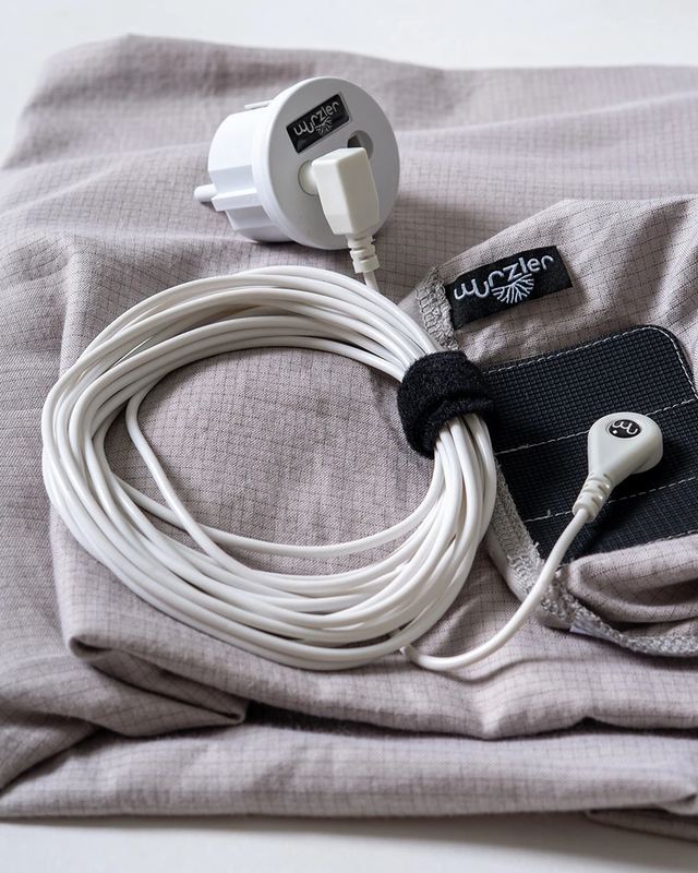 Zusammengerolltes Anschlusskabel des Erdungsbettlakens mit Stecker, Steckdosenadapter und Anschlusspad auf dem gefalteten Laken